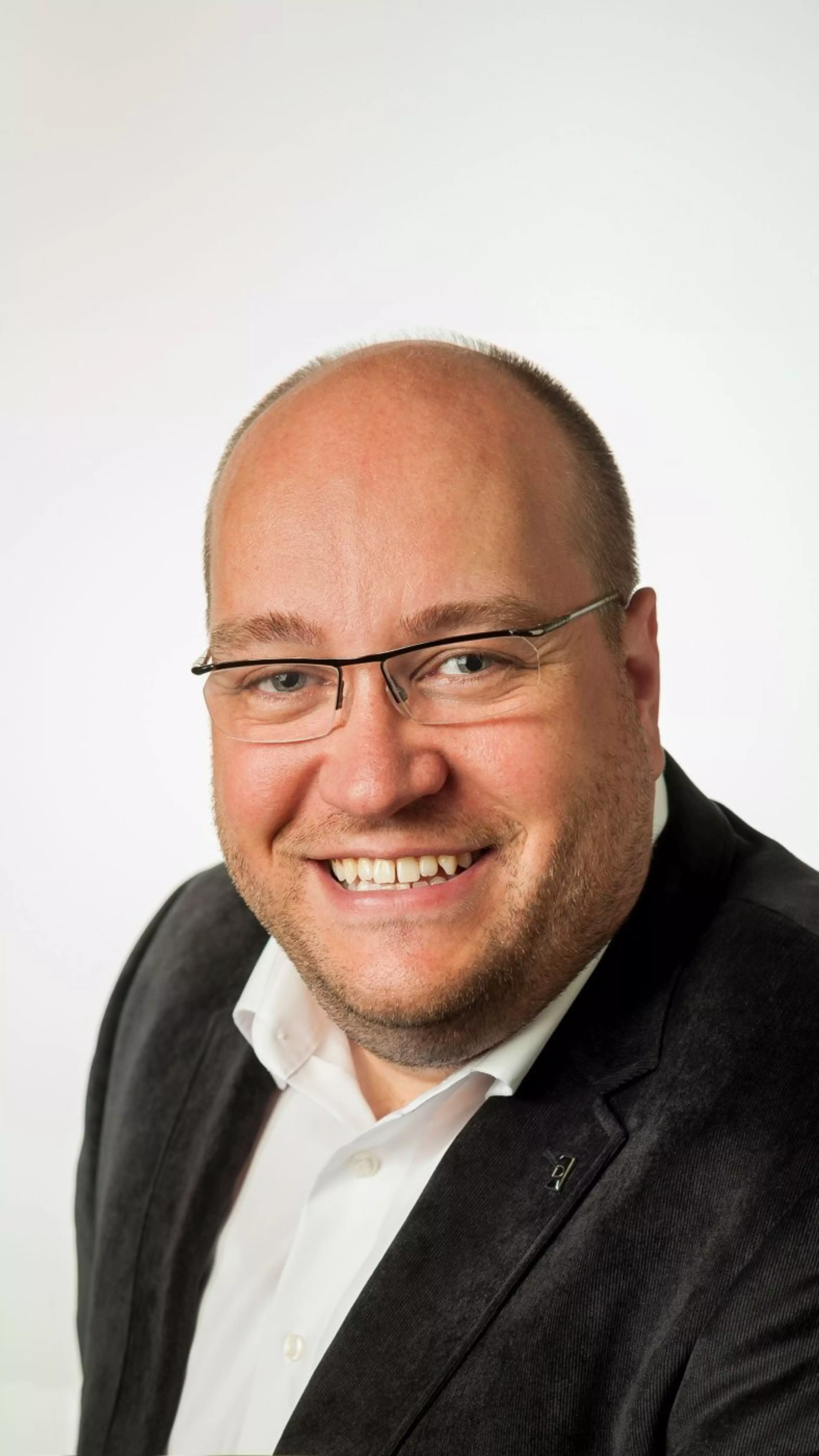 Porträt von Martin Wendring, Marketingleiter der SETEX-Textil GmbH, lächelnd mit Brille, im dunklen Sakko und weißem Hemd vor hellem Hintergrund.