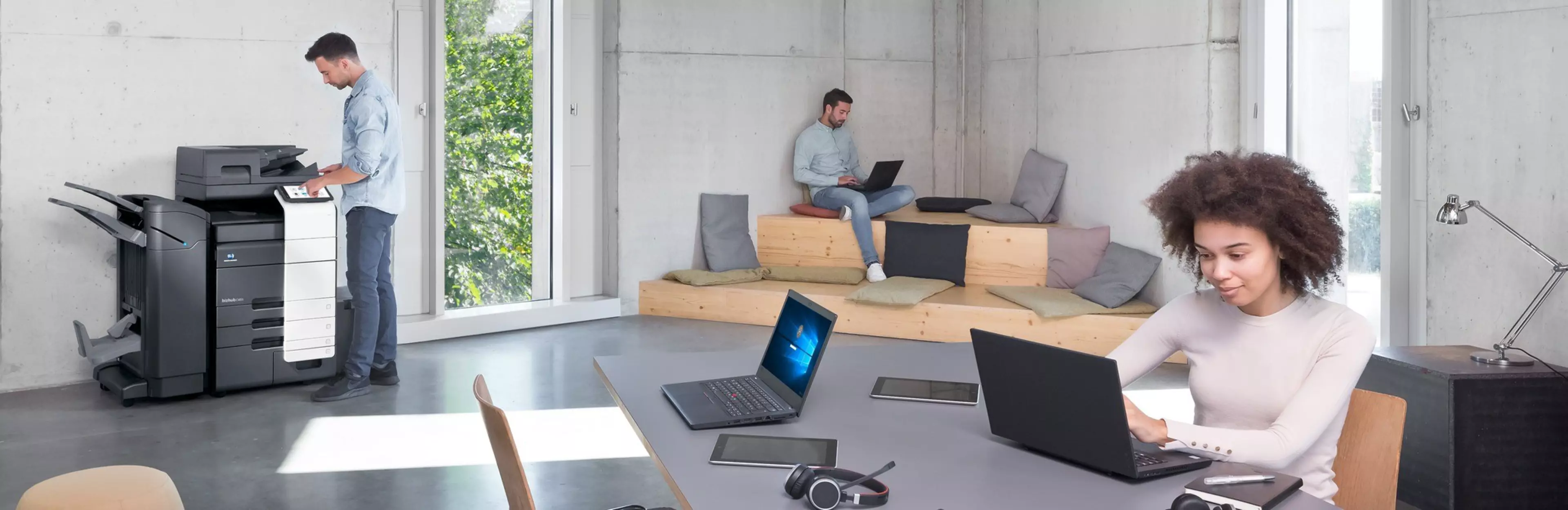 Flexible working in a modern office: employees use laptops and multifunction printers. Supported by the Universal Print Driver from Konica Minolta.