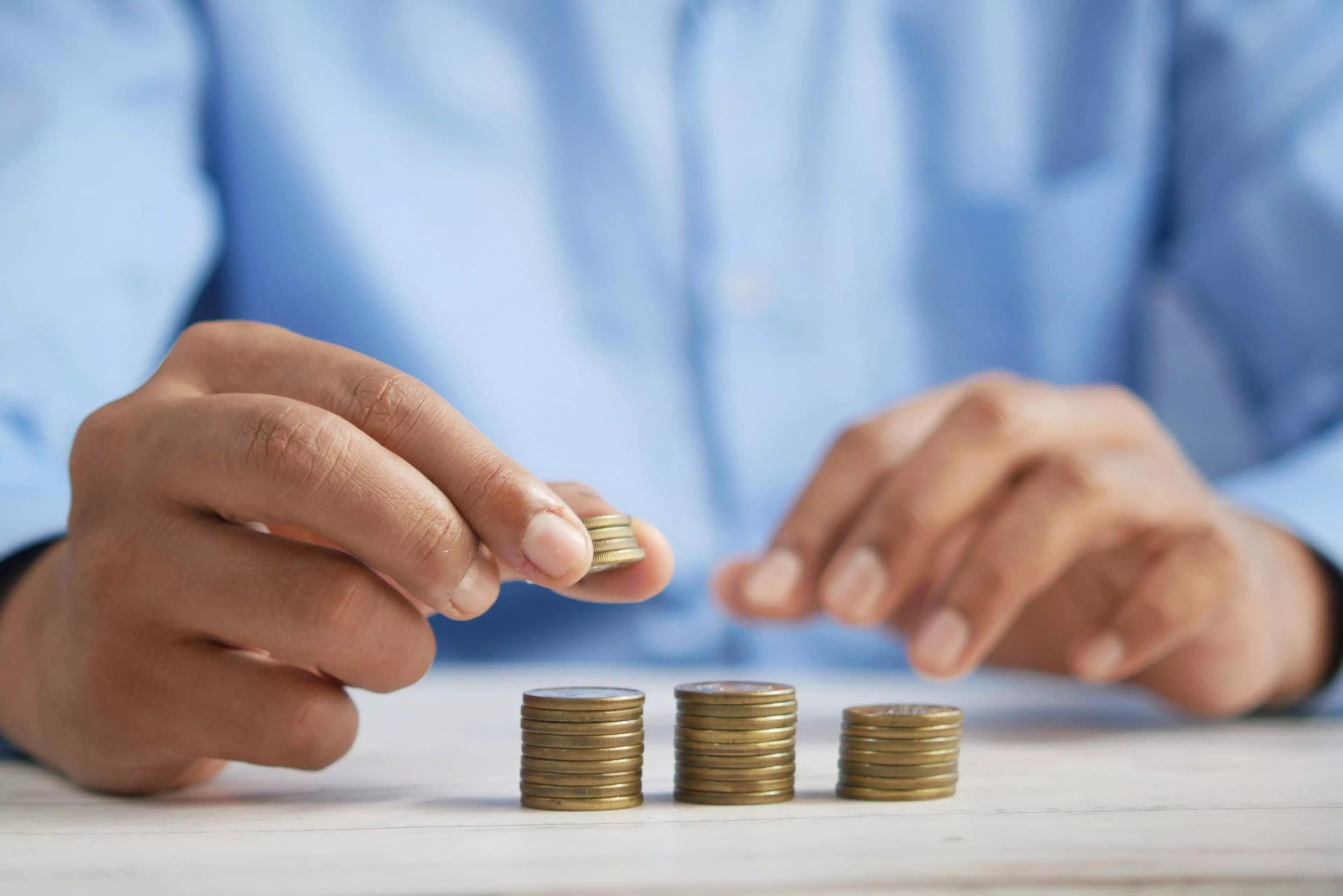 Manos de un hombre en una oficina haciendo montoncitos de monedas sobre una mesa