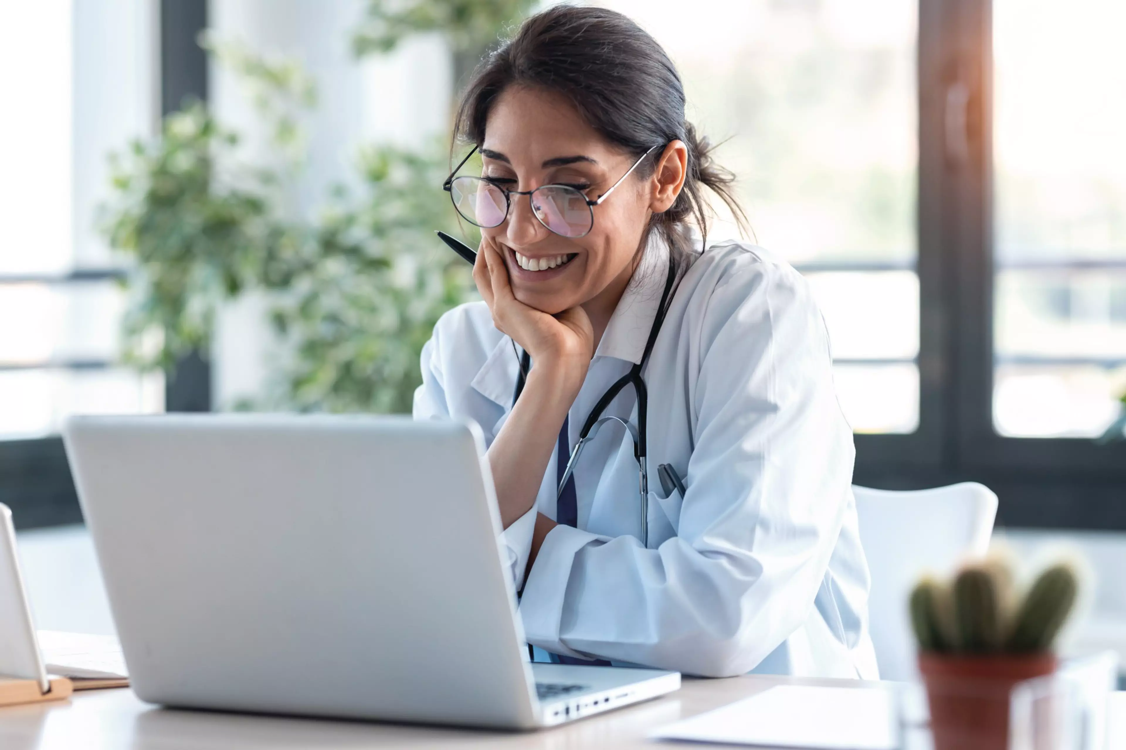 Shot of smiling female doctor working with her laptop in the consultation.