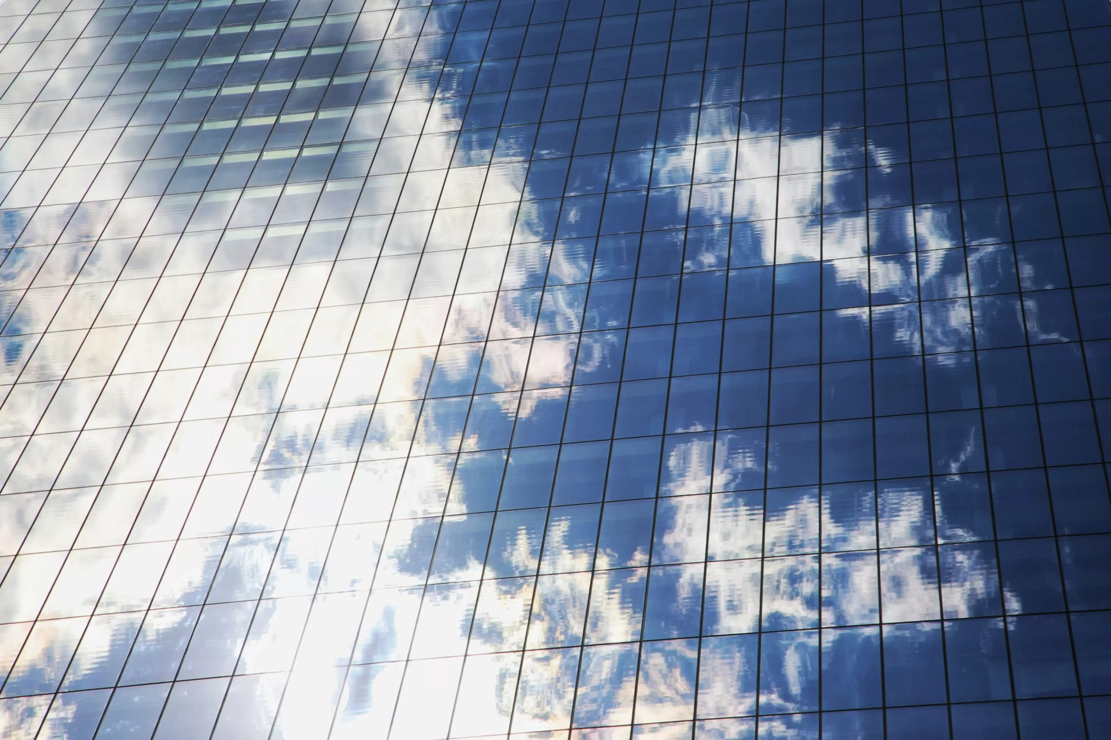 El cielo con algunas nubes blancas se refleja en la fachada de un edificio.