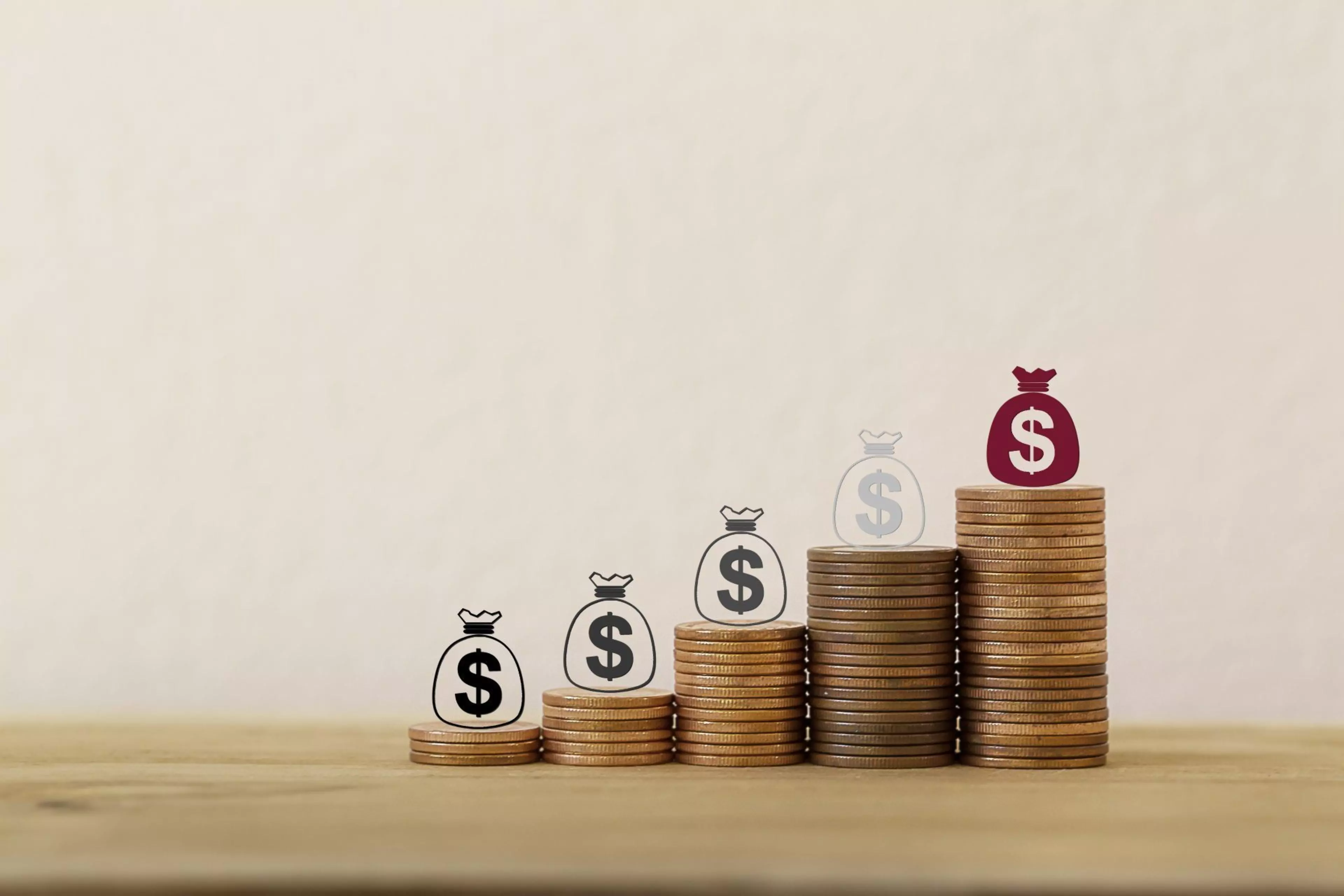 Gestapelte Münzen in aufsteigender Höhe mit Symbolen von Geldsäcken, die wachsendes Kapital und steigende Investitionen darstellen.
