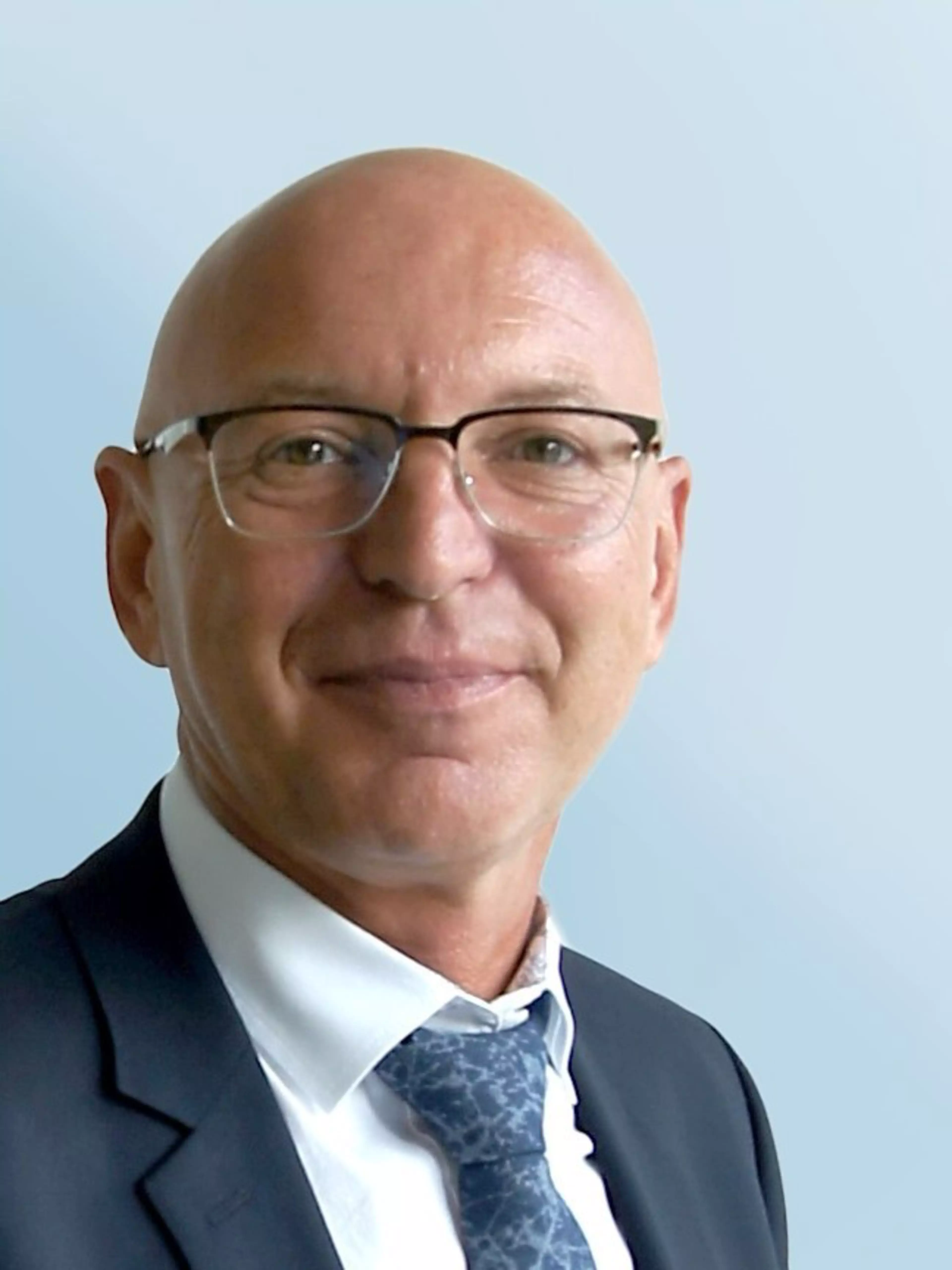 Porträt von Wolfgang Ilbertz, Business Development Manager bei Konica Minolta, im Anzug mit gemusterter Krawatte vor hellblauem Hintergrund