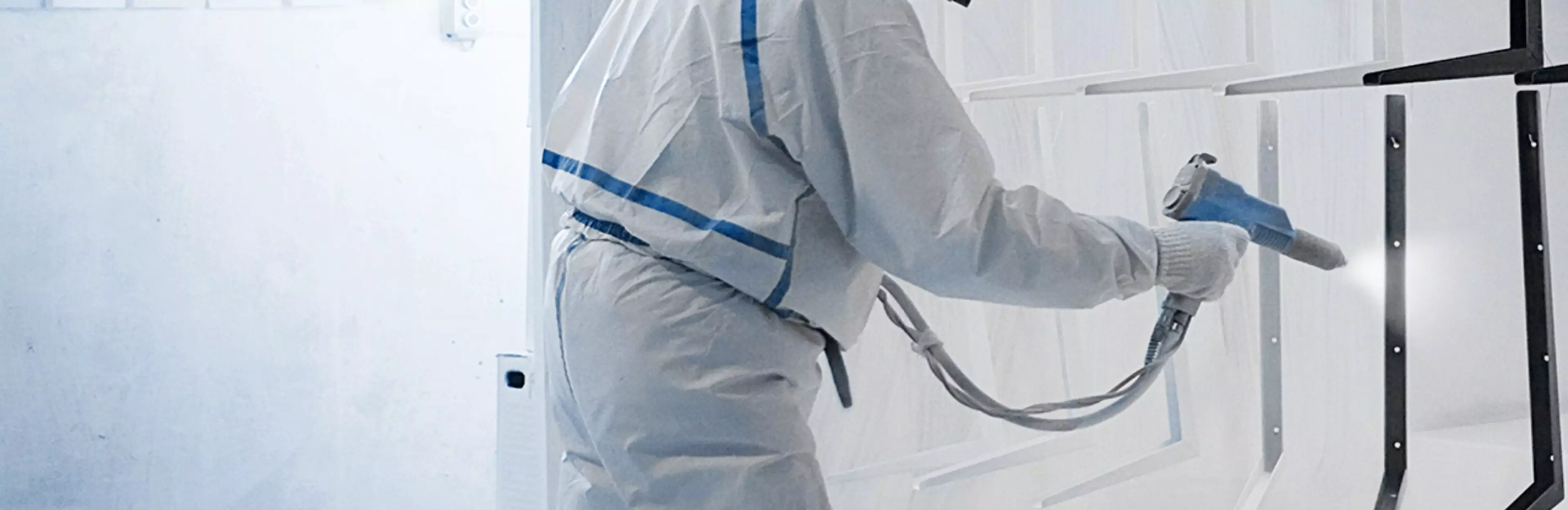 Worker is powder coating some parts in a spray booth