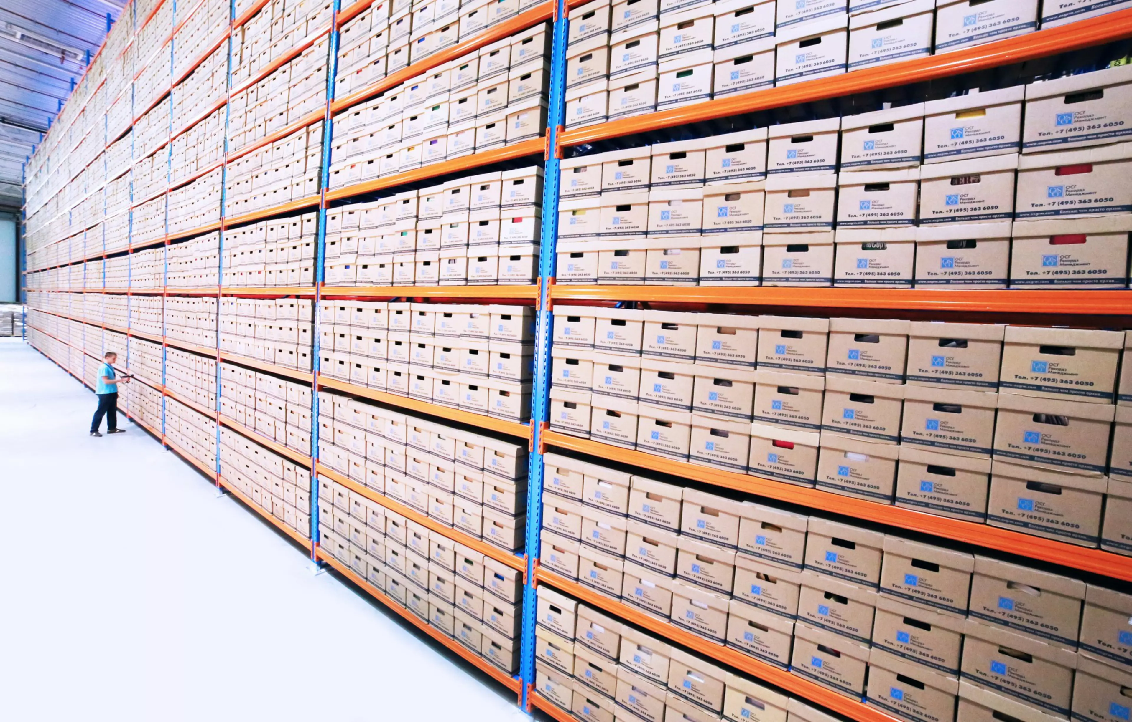 Enorme almacén de cajas llenas de documentos en papel, y un trabajador muy pequeñito enfrentándose a ellas