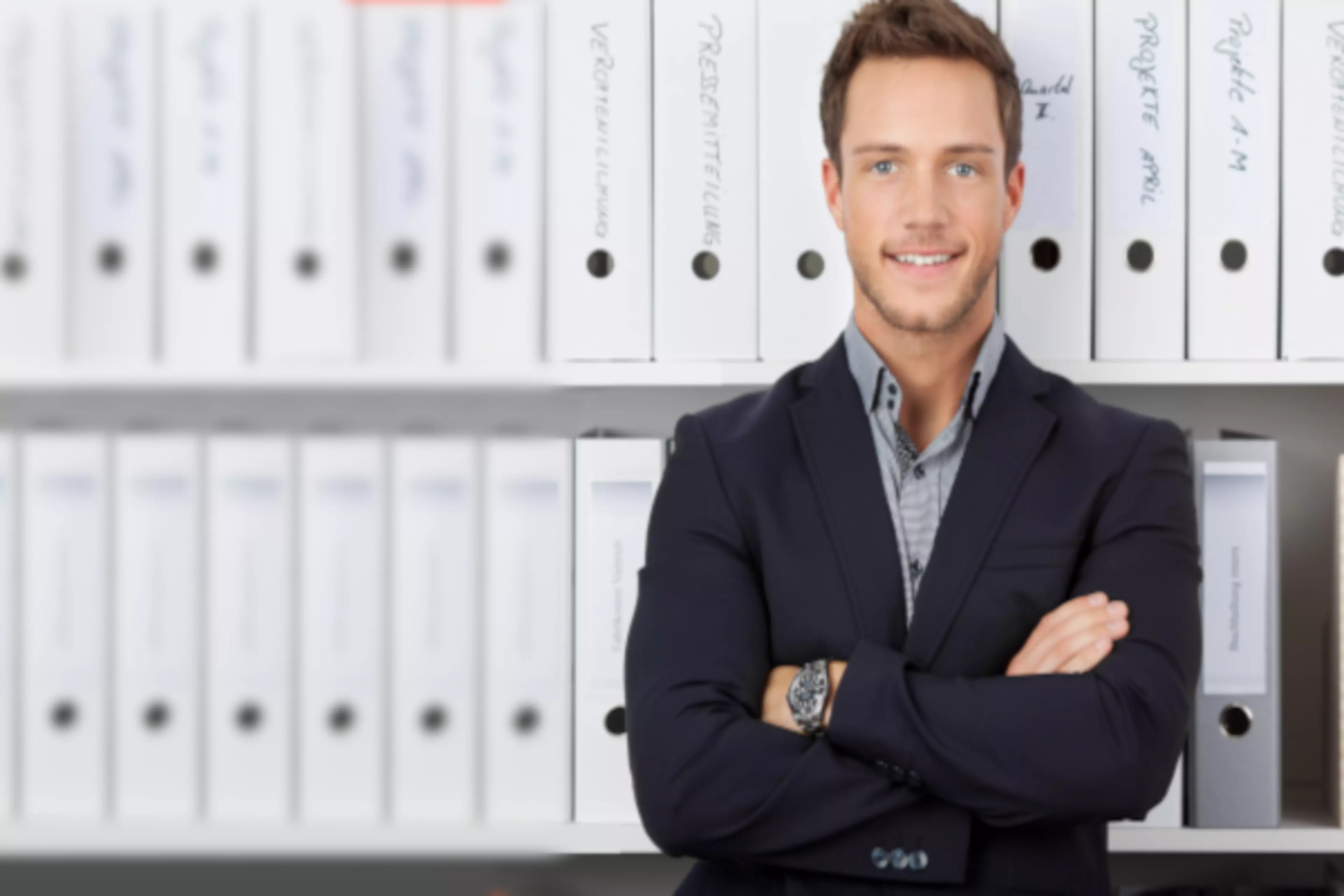 Un hombre con los brazos cruzados frente a una estantería llena de archivadores