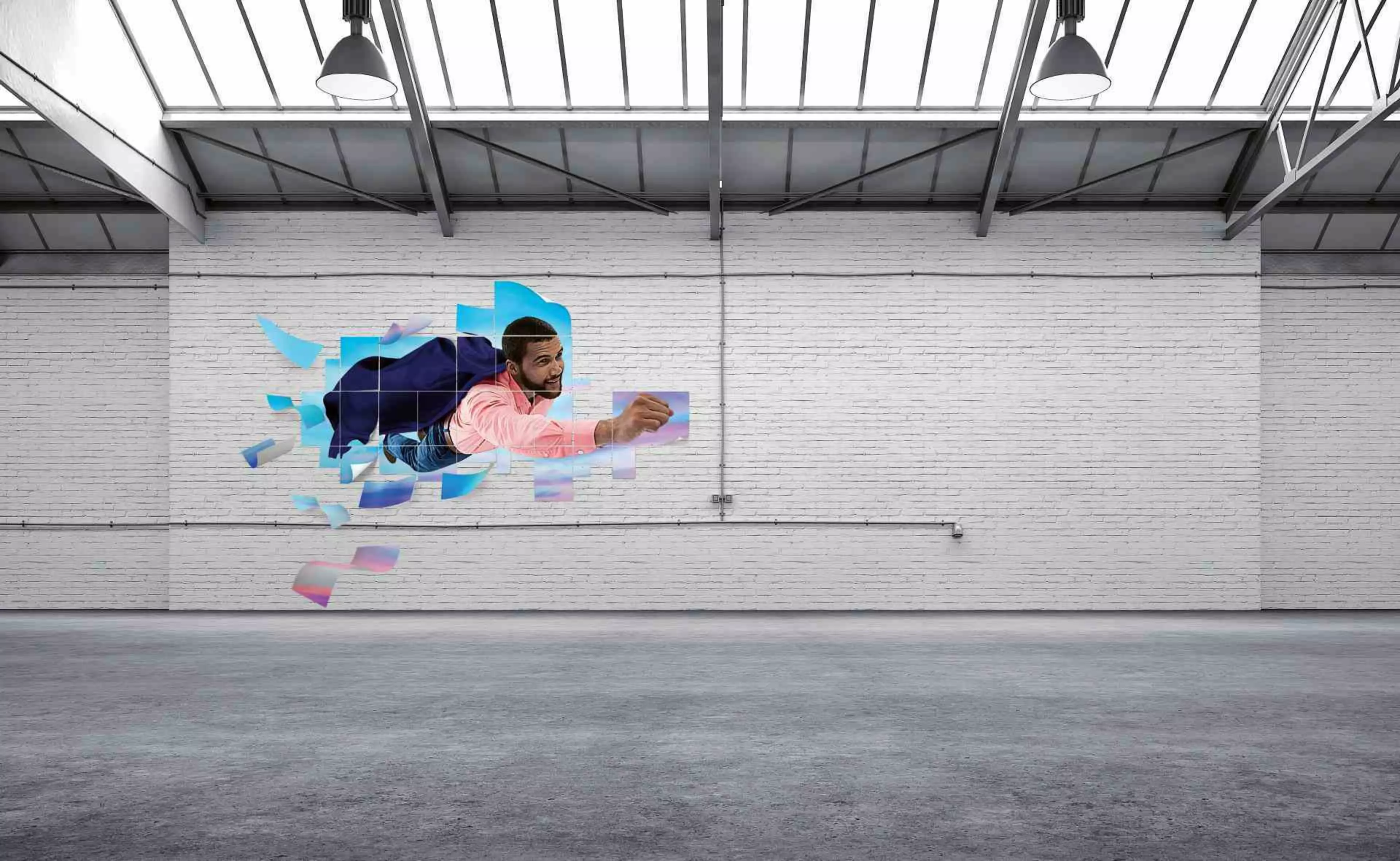 Leere Industriehalle mit weißer Ziegelwand und Dachfenstern; an der Wand ein farbiges Motiv eines schwebenden Mannes, der durch digitale Papierfragmente fliegt.