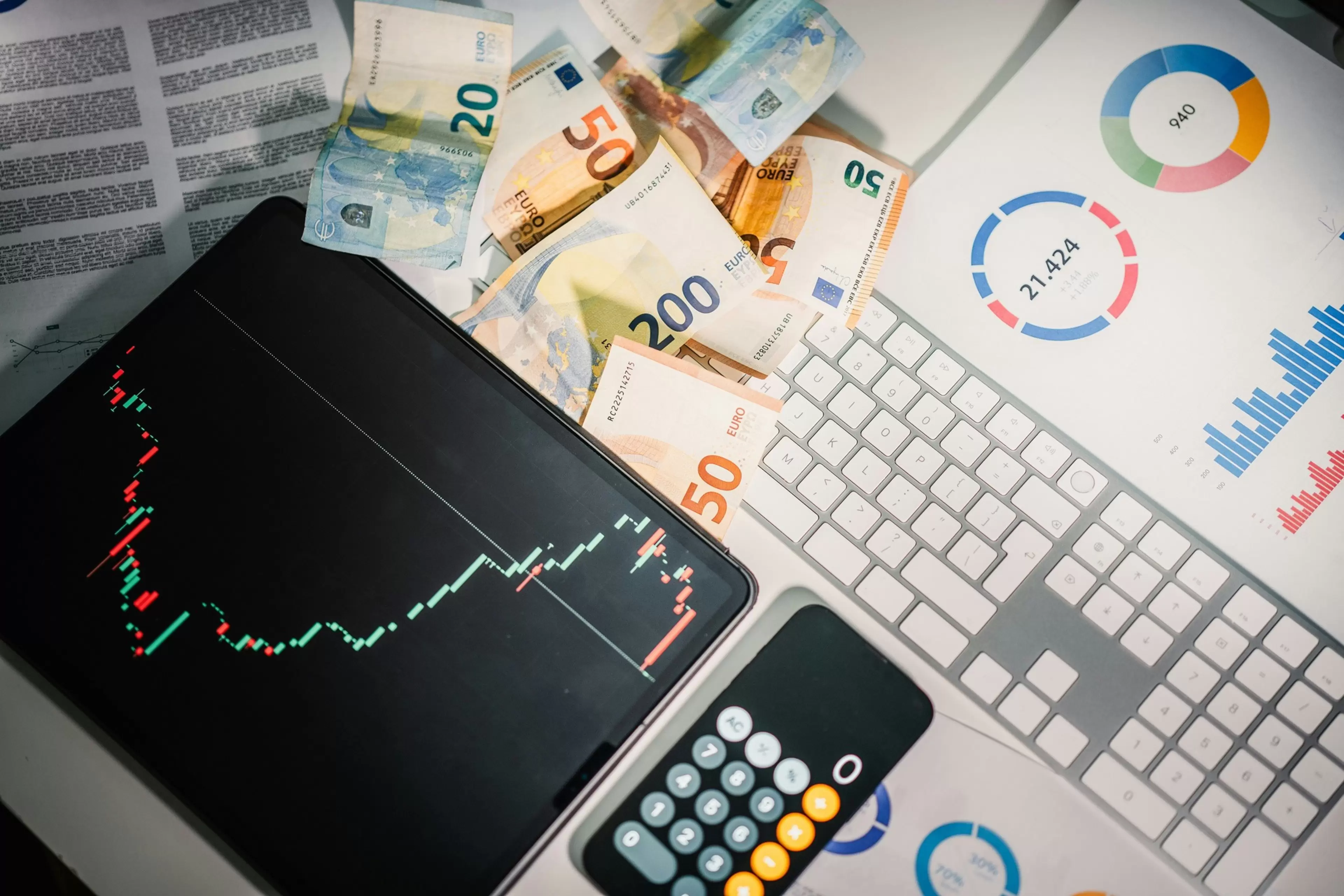 Tablet, calculadora y teclado de ordenador sobre papeles con gráficas económicas