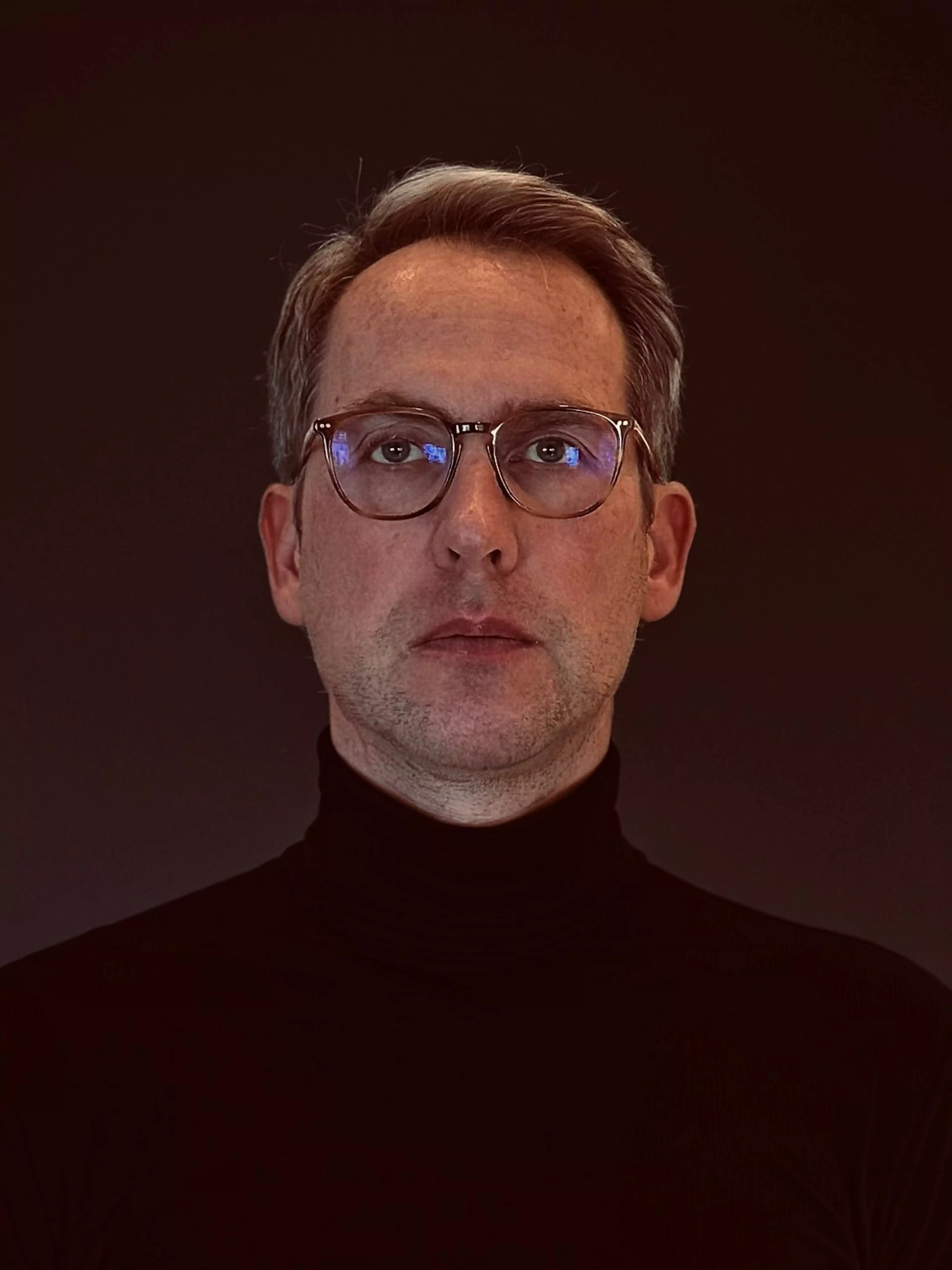 Porträt von Lutz Wolter, Senior Expert Leasing Program bei Konica Minolta, mit Brille und schwarzem Rollkragenpullover vor dunklem Hintergrund.