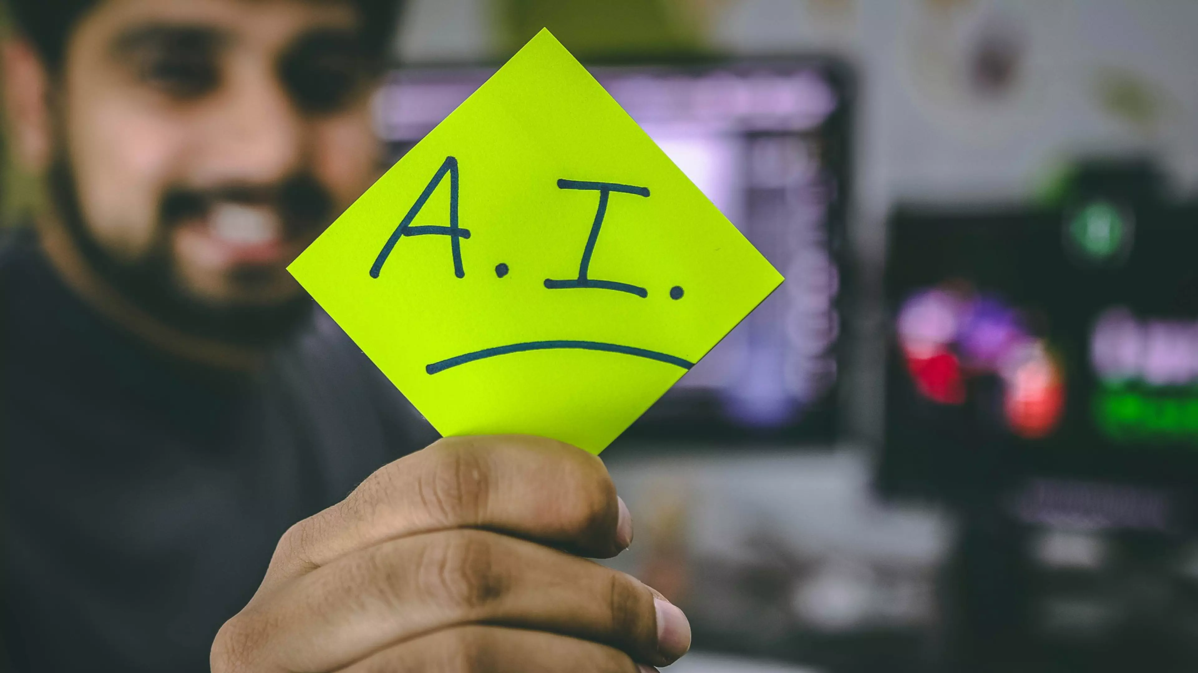 Un hombre joven y sonriente mostrando un post-it en el que pone «A.I.»
