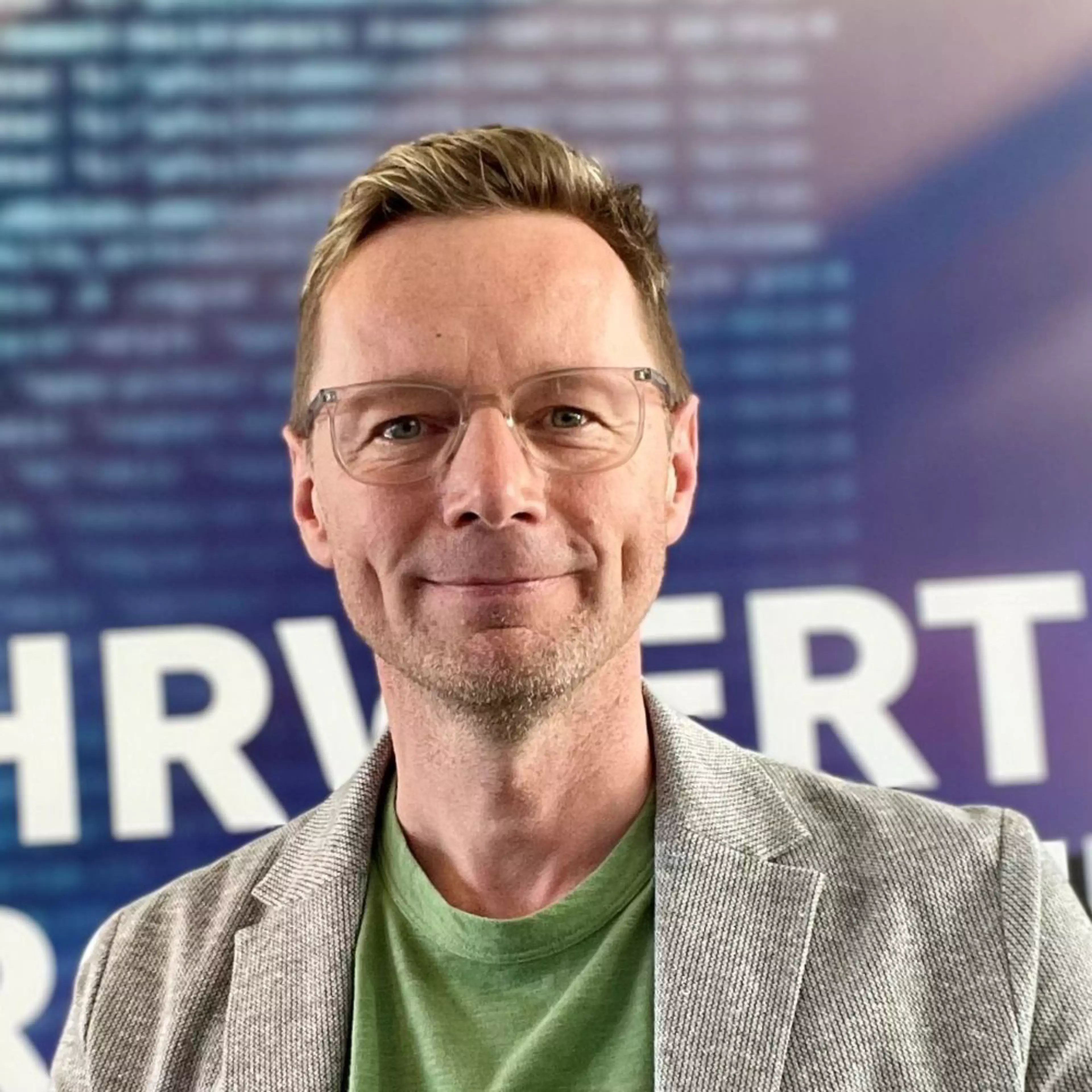 Porträt von Andreas Knobloch, Senior Account Manager Business Software bei Konica Minolta Deutschland, mit Brille vor einem blau-violetten Hintergrund mit Schrift.