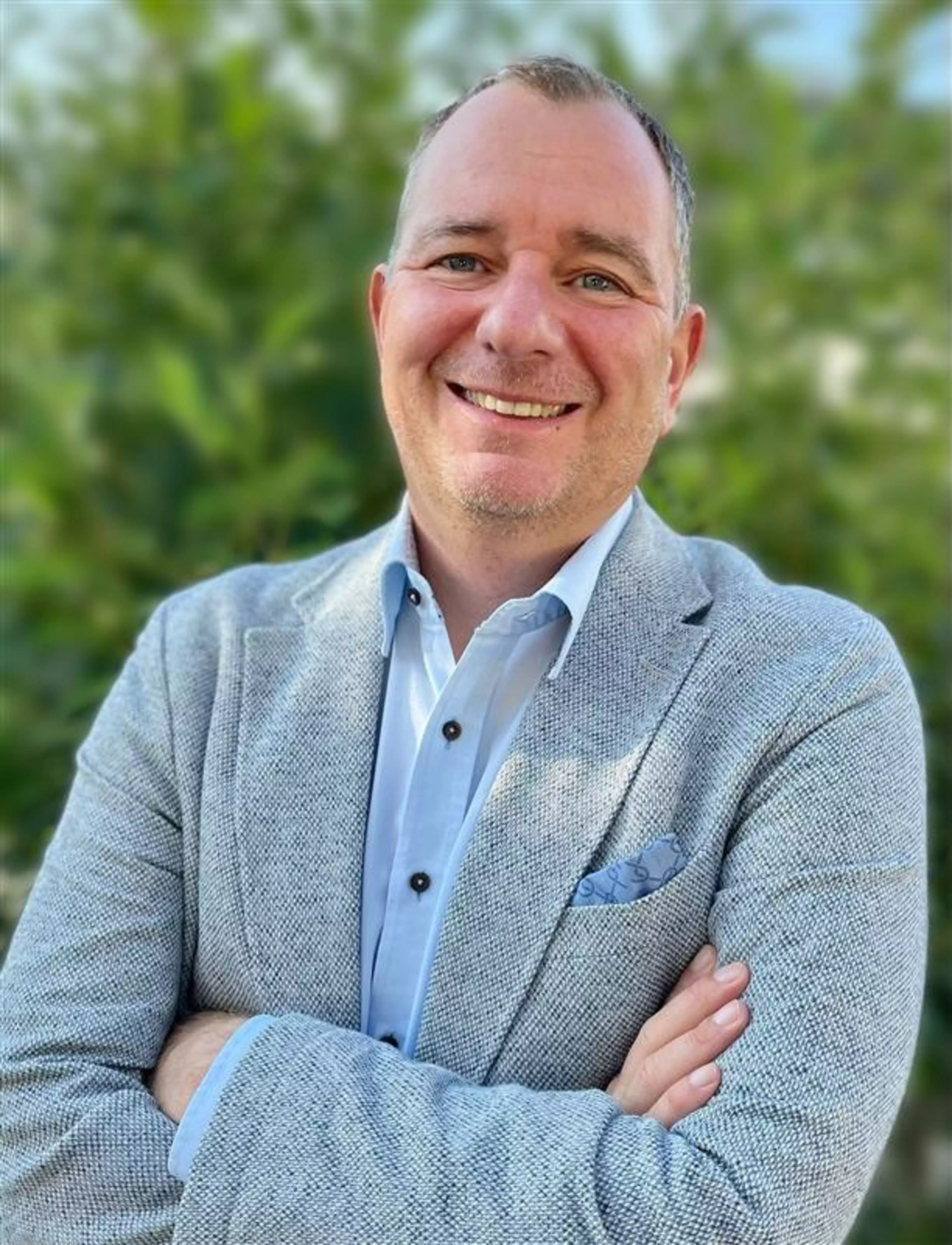 Porträt von Wolfgang Sageder, Leiter Team Kirche & Soziales bei Konica Minolta Deutschland, lächelnd vor grünem Hintergrund.