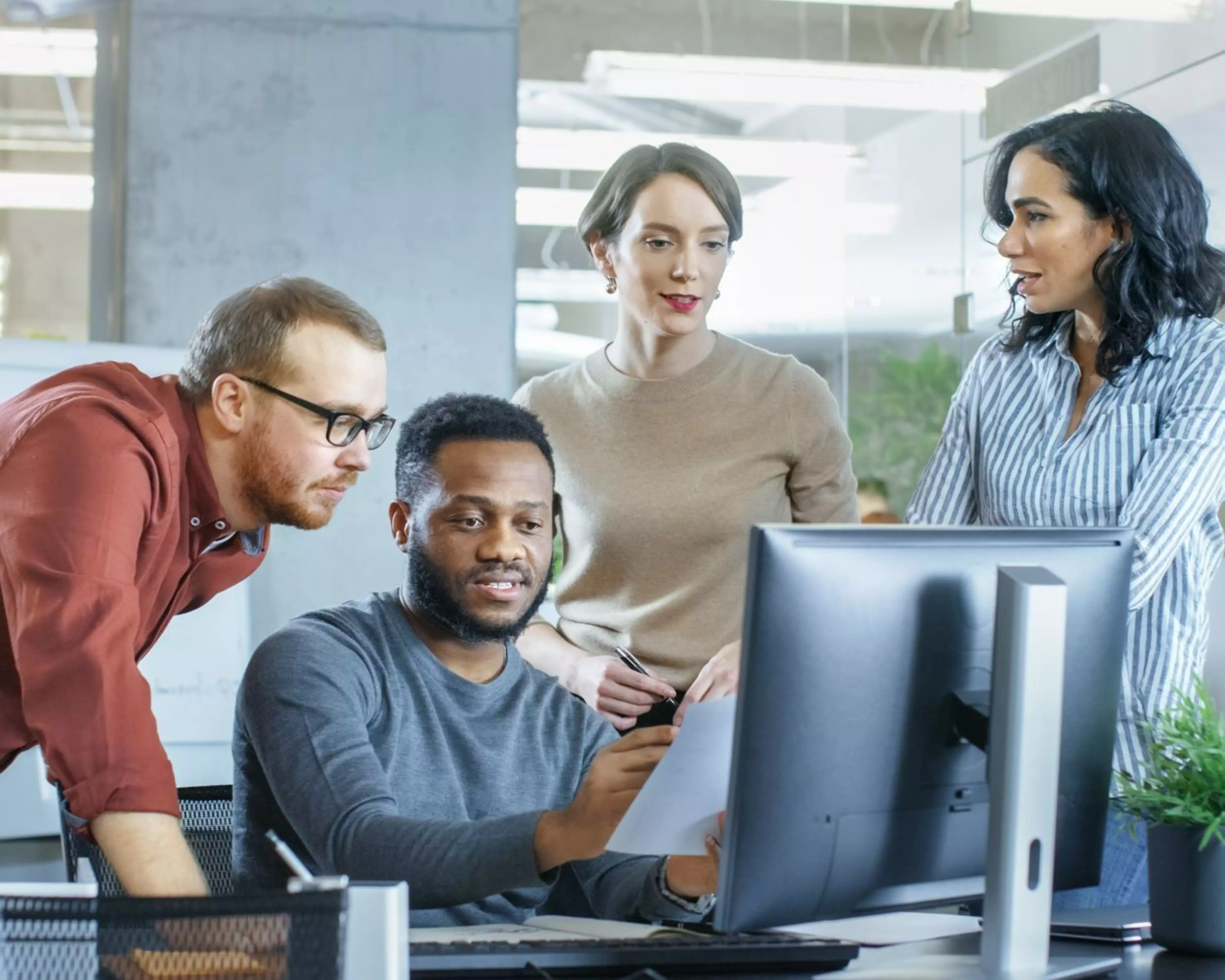Team aus vier Personen arbeitet gemeinsam an einem Bildschirm – symbolisiert Wissensaustausch, kollegiale Beratung und Zusammenarbeit
